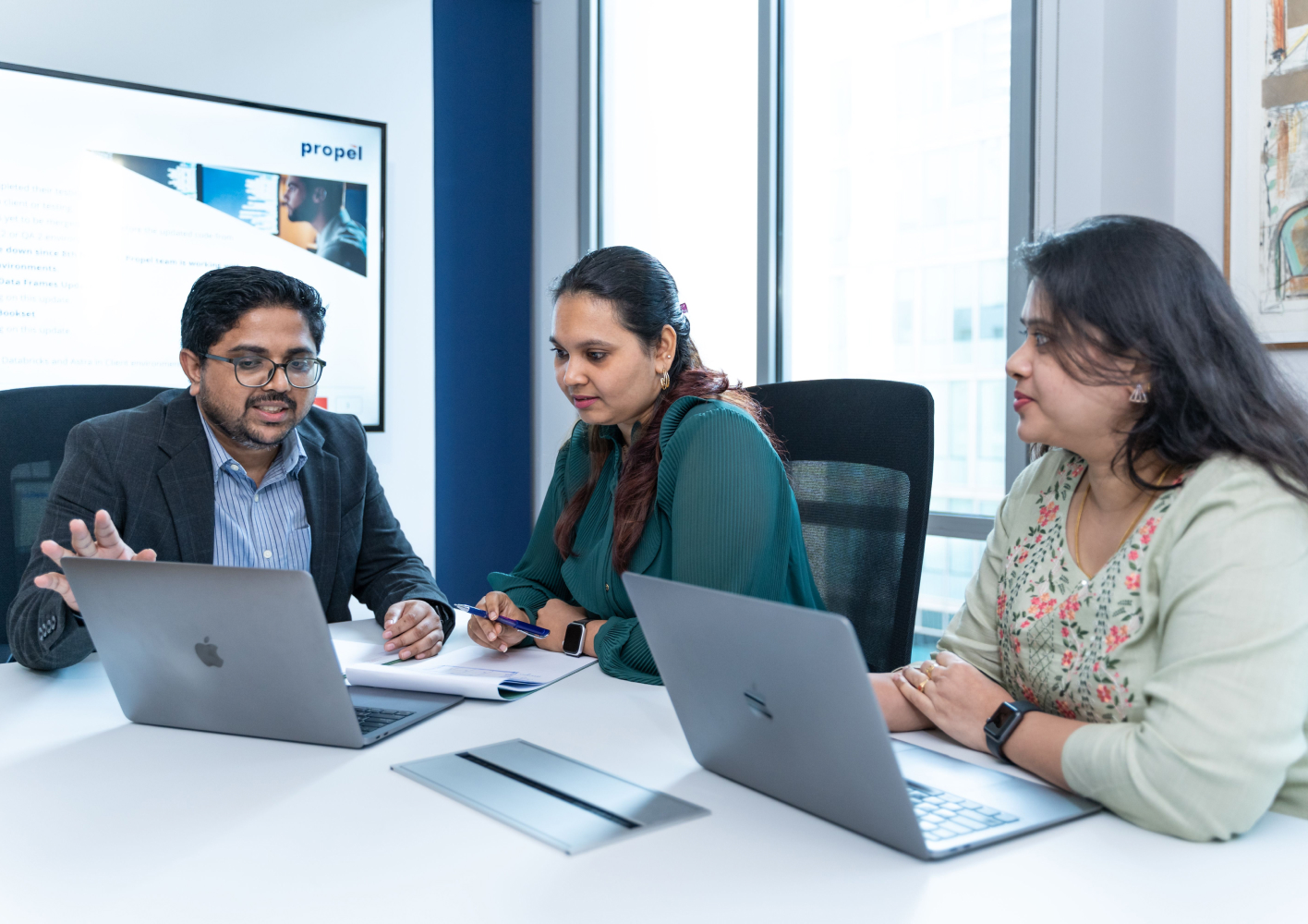 Three colleagues reviewing work on laptops in a meeting
