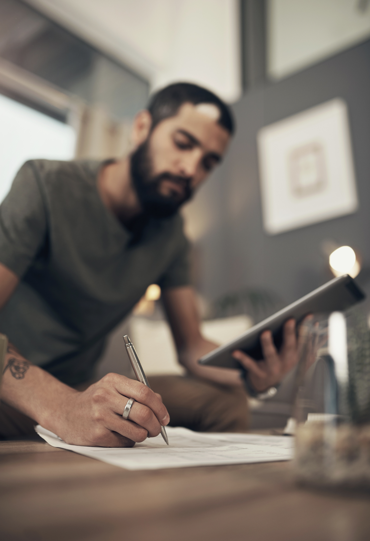 Man writing on paper while holding a tablet
