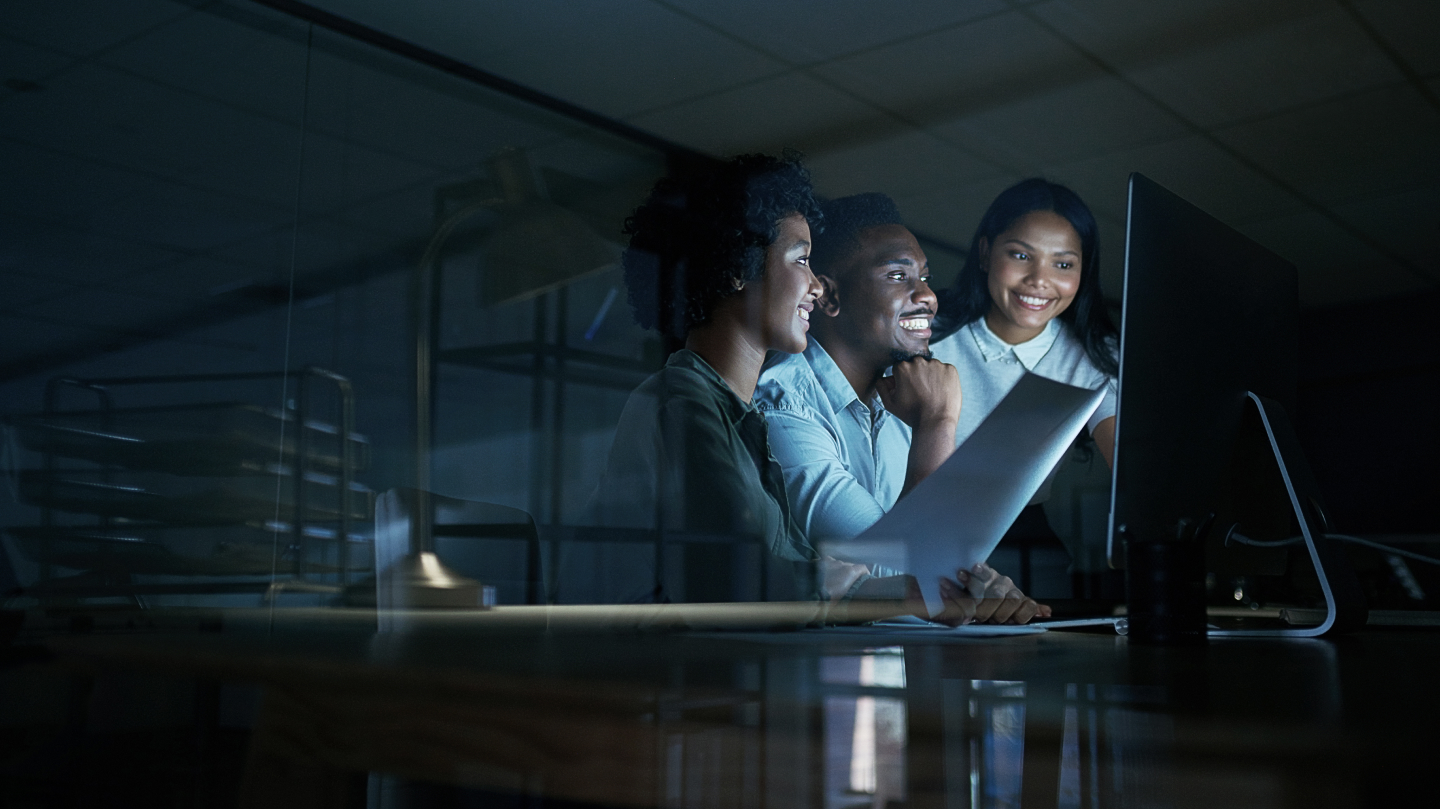 Three colleagues looking at a laptop in a dim room
