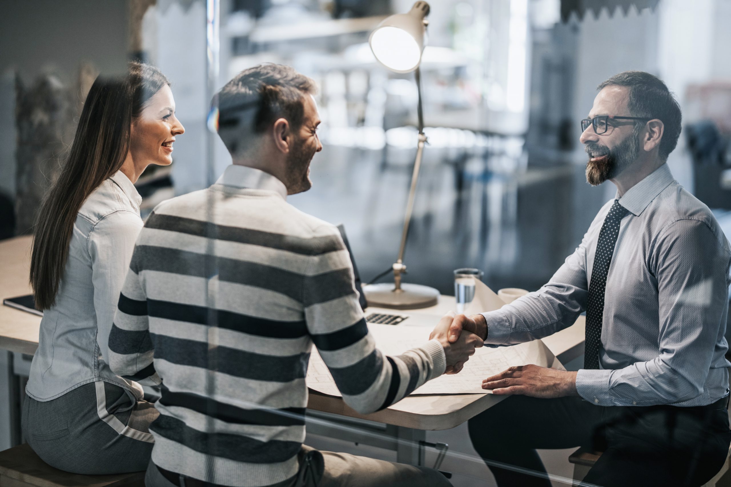 Two people shaking hands across a desk during a meeting