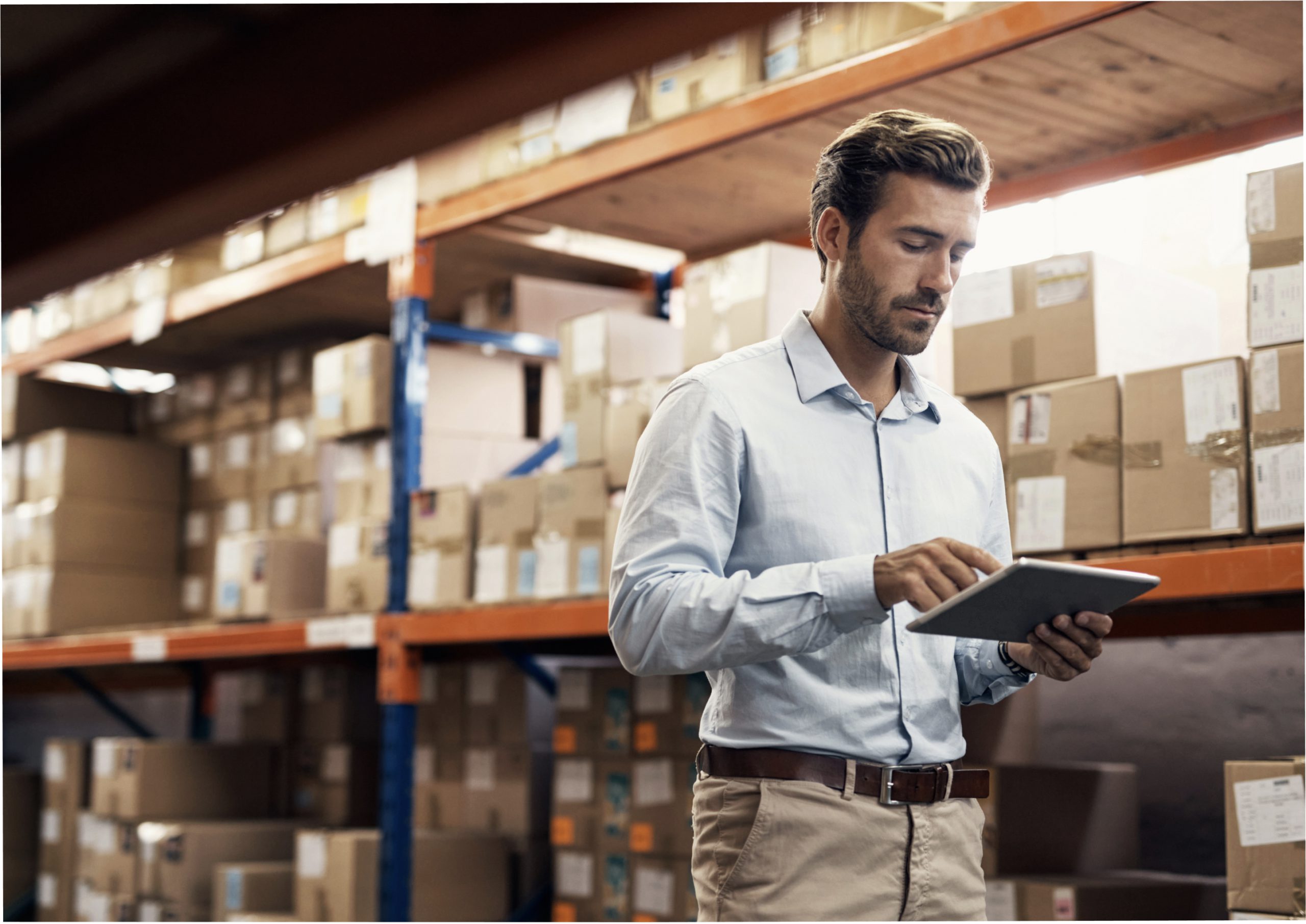 Warehouse worker checking a tablet beside shelves of boxes