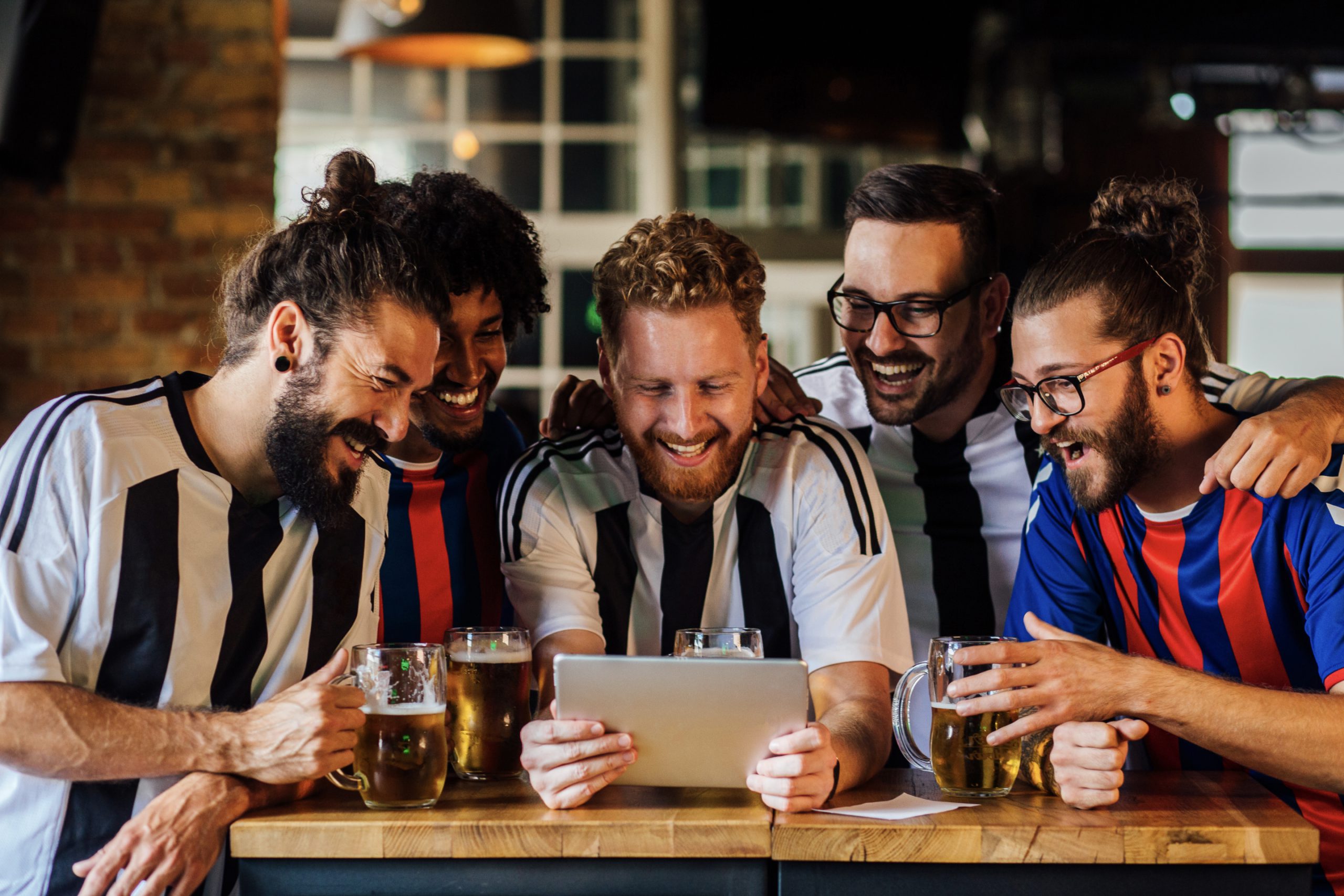 Friends cheering while watching a match on a tablet in a bar