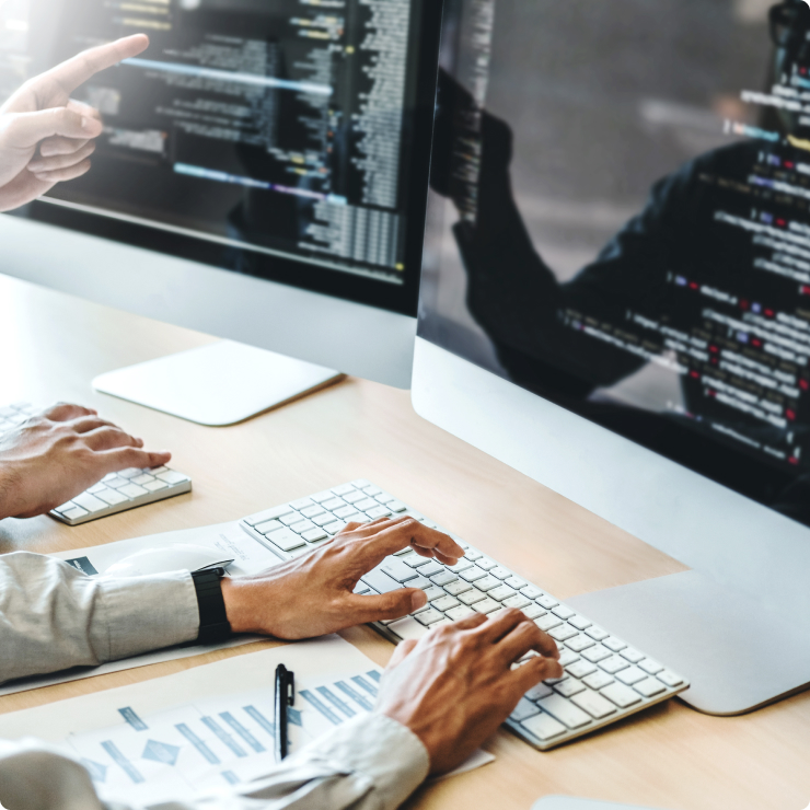 Hands typing on a keyboard beside a monitor showing code