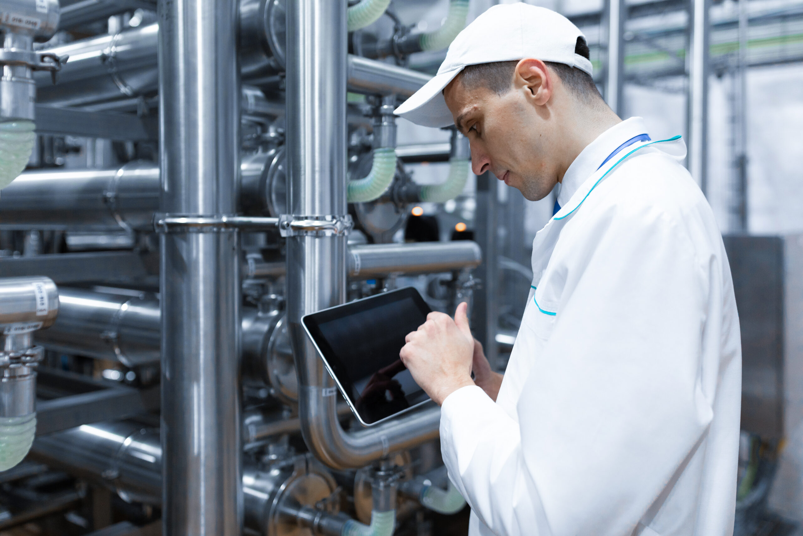 Technician in a white coat checking a tablet beside factory equipment