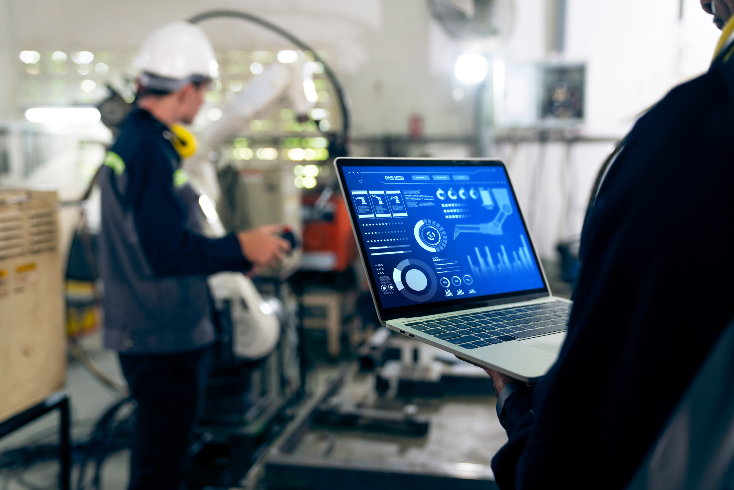 Factory workers monitoring a robotic arm on a laptop