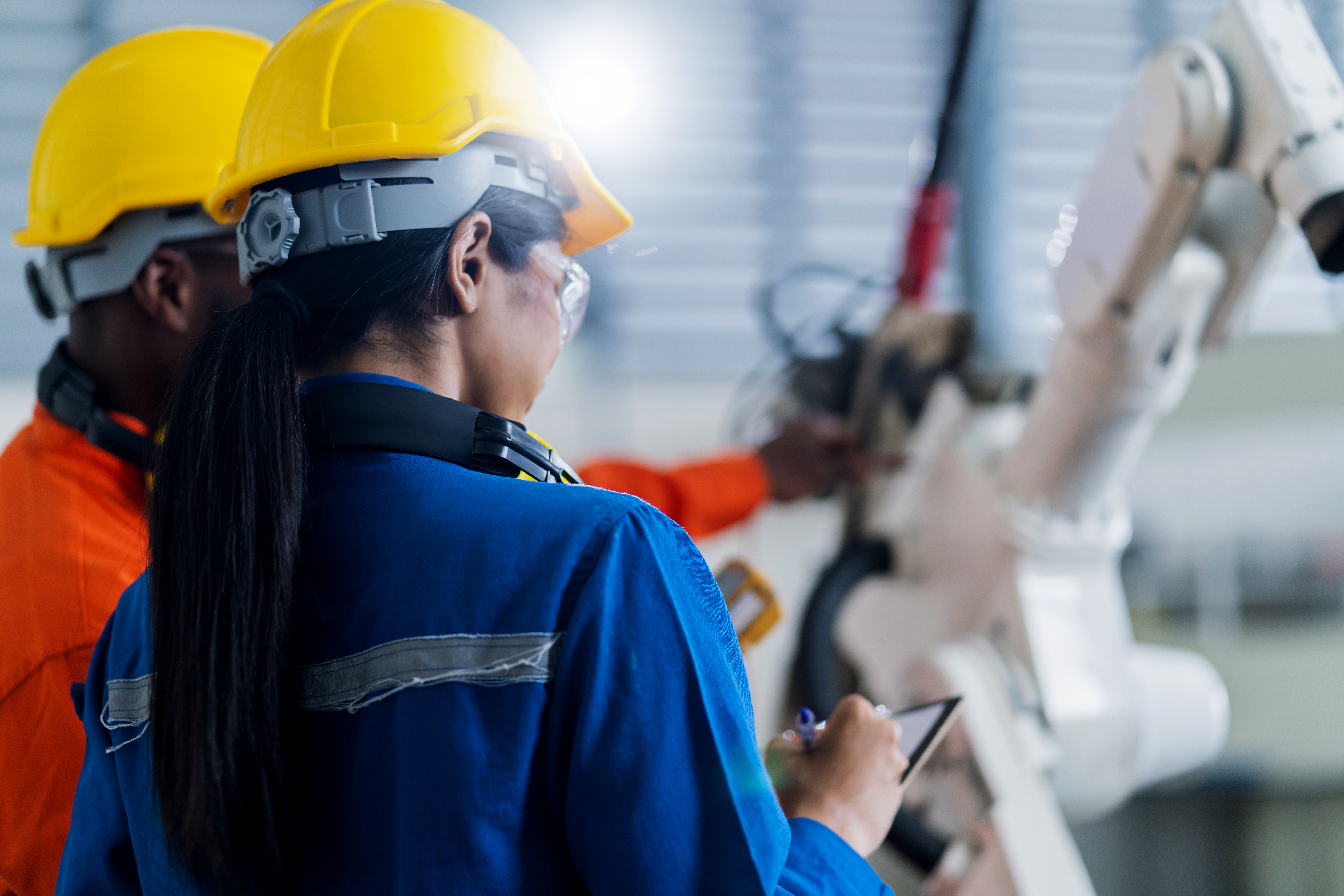 Two workers in hard hats watching a robotic arm