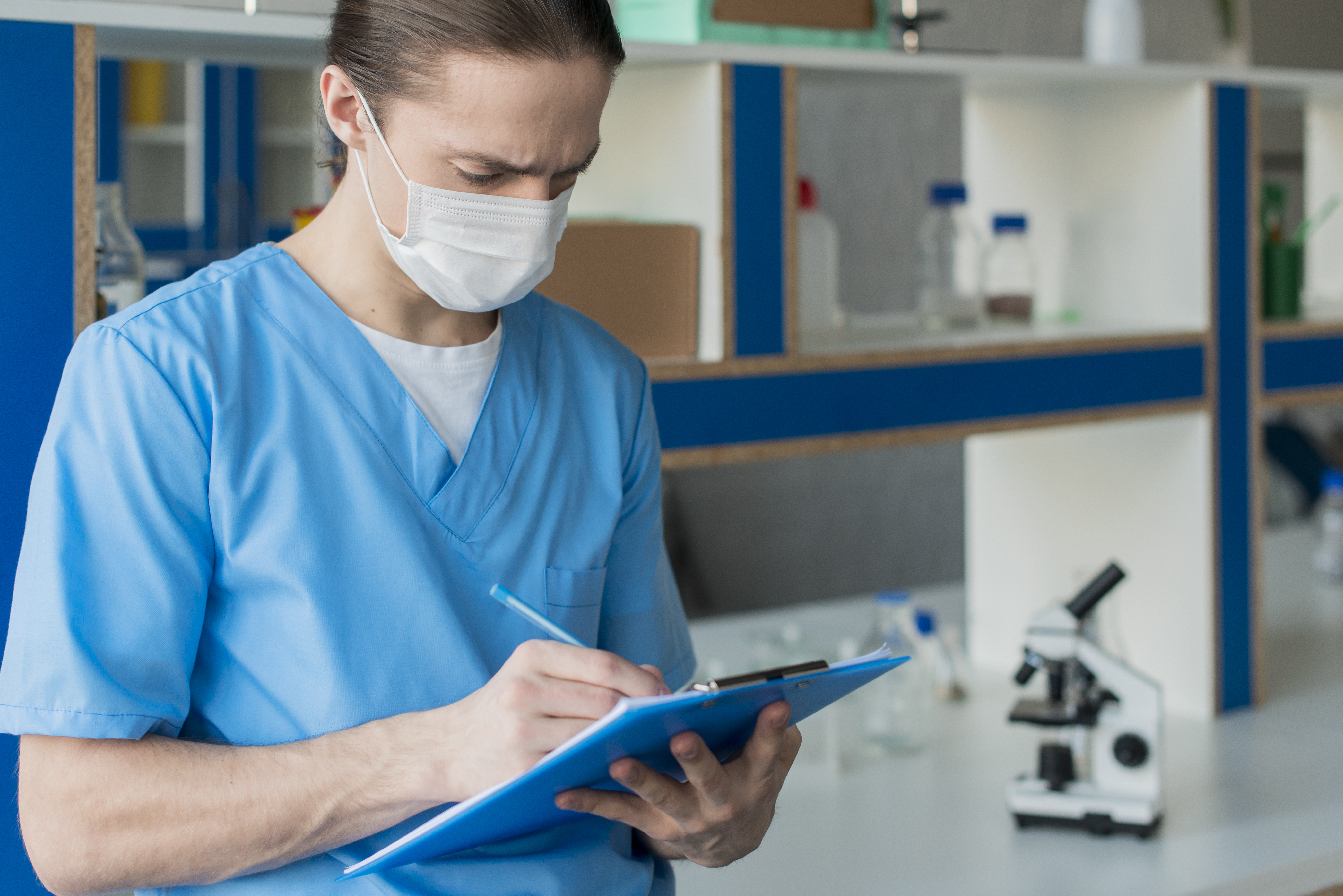 Nurse in scrubs and a face mask holding a clipboard in a lab