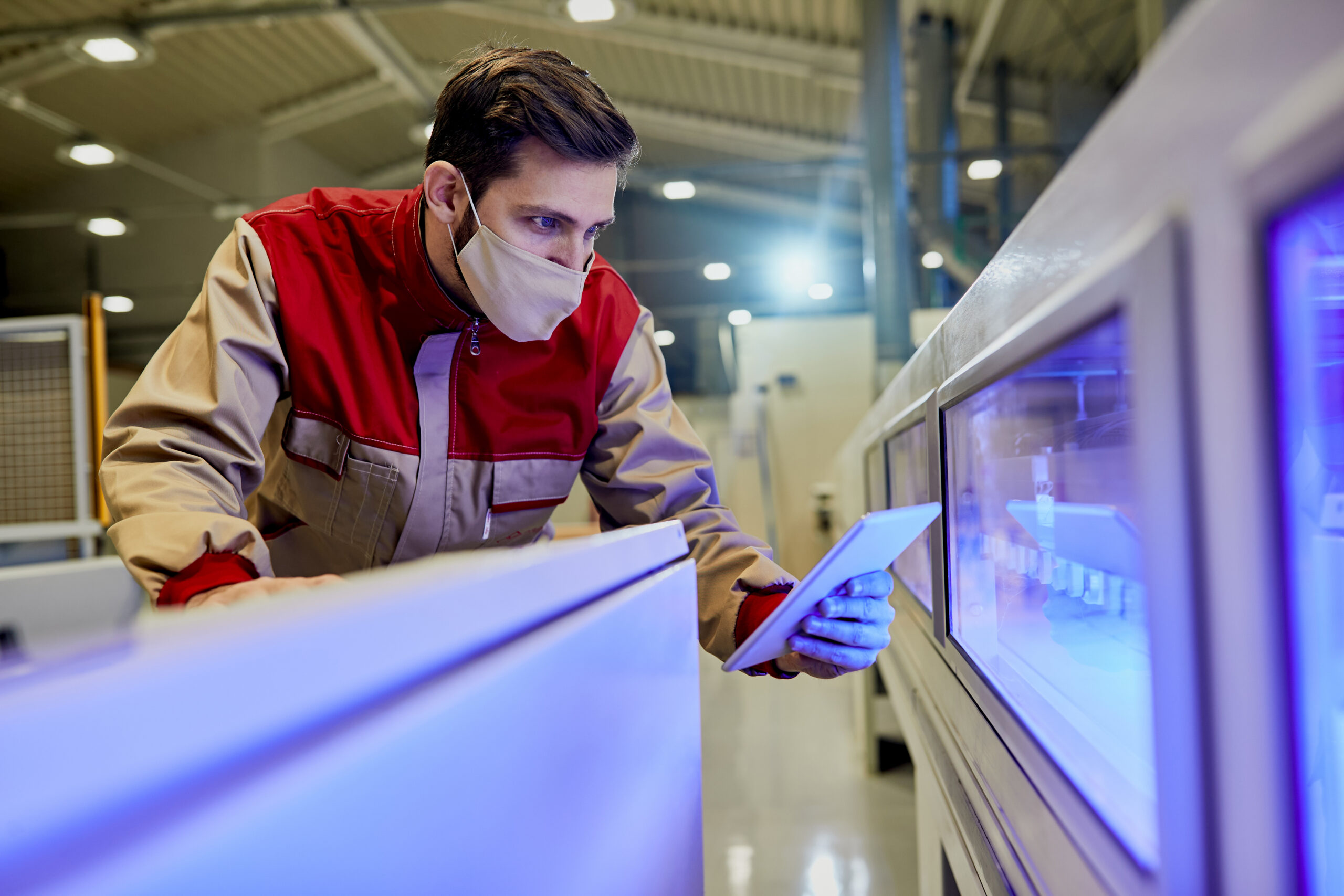 Factory operator in a face mask checking a machine on a tablet