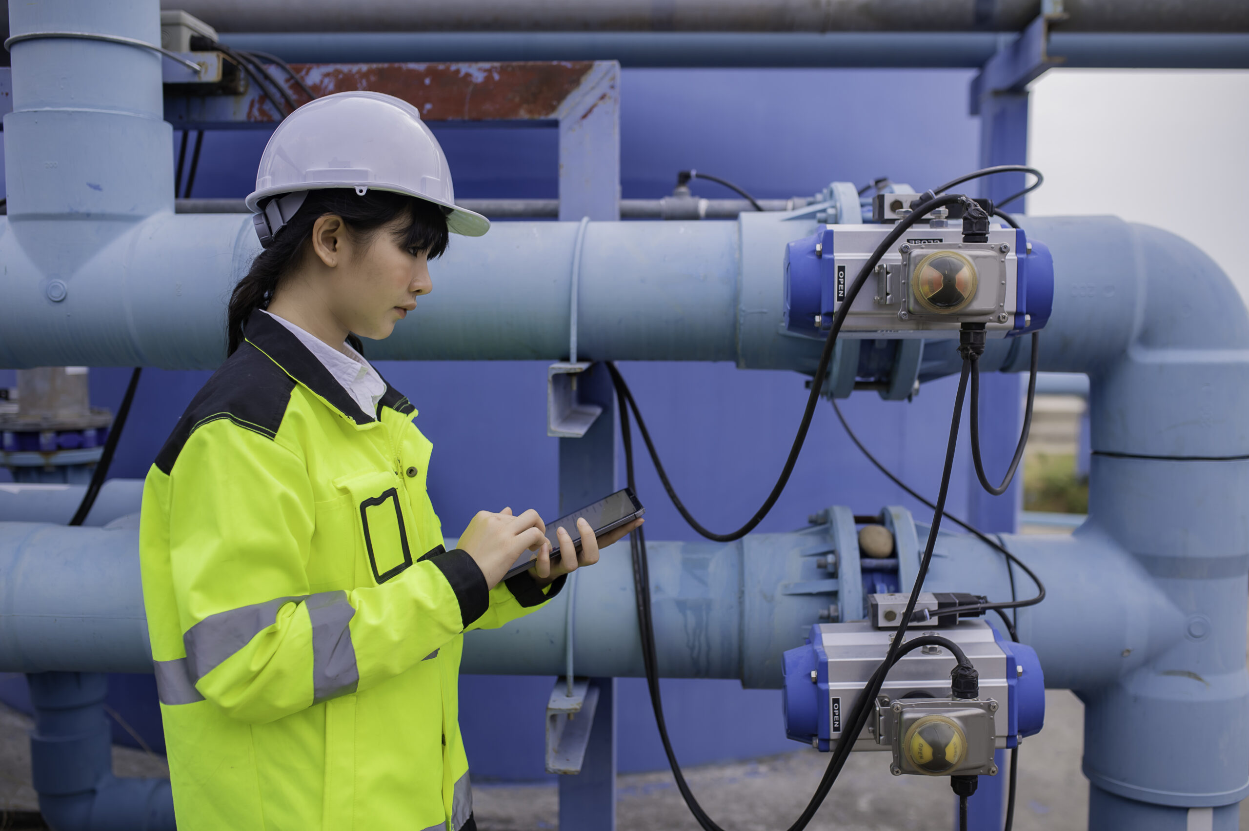 Engineer in a hard hat and hi-vis vest with a tablet beside pipes