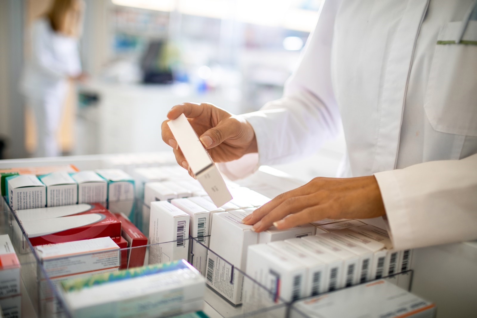 Pharmacist's hand holding a pill beside medication packs